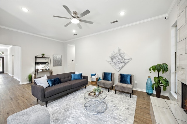 living room featuring ceiling fan, ornamental molding, wood-type flooring, and a high end fireplace