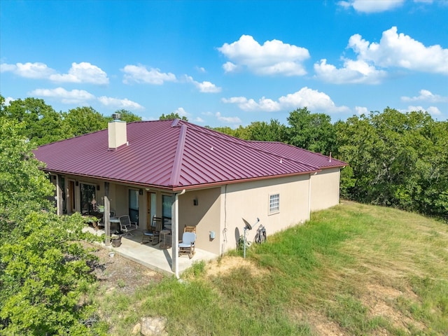 rear view of house featuring a patio area, a chimney, stucco siding, metal roof, and a yard