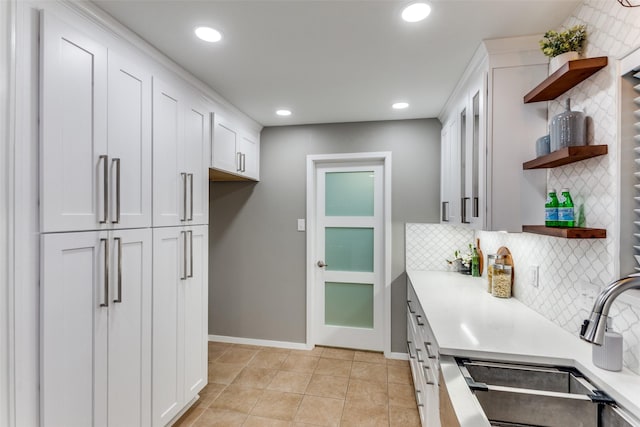 kitchen featuring backsplash, light tile patterned floors, sink, and white cabinets