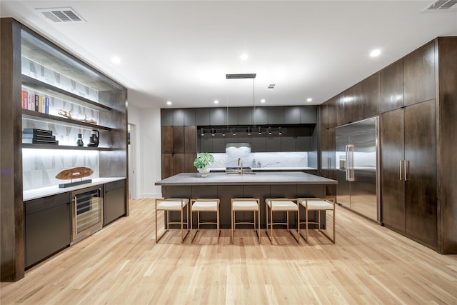 kitchen with dark brown cabinets, wine cooler, built in refrigerator, a breakfast bar area, and modern cabinets