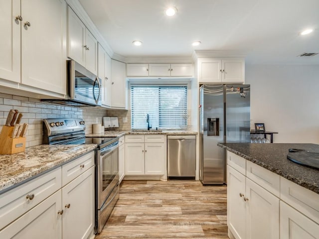 kitchen with sink, white cabinetry, backsplash, stainless steel appliances, and light stone countertops