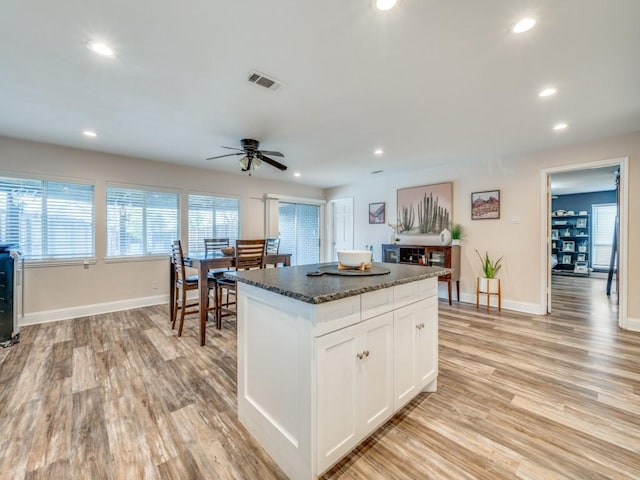 kitchen featuring white cabinetry, light hardwood / wood-style flooring, dark stone countertops, a kitchen island, and ceiling fan