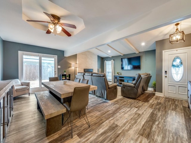 dining area with lofted ceiling with beams, ceiling fan with notable chandelier, a healthy amount of sunlight, and hardwood / wood-style floors