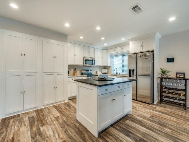 kitchen featuring white cabinetry, stainless steel appliances, light hardwood / wood-style floors, and dark stone countertops