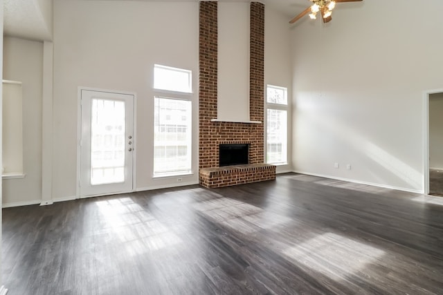 unfurnished living room featuring dark hardwood / wood-style floors, a towering ceiling, a fireplace, and ceiling fan