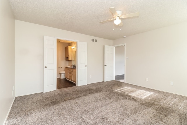 unfurnished bedroom featuring ceiling fan, ensuite bath, dark carpet, and a textured ceiling