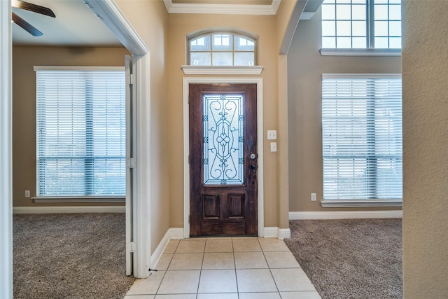 foyer entrance with ornamental molding, carpet flooring, ceiling fan, and tile patterned floors