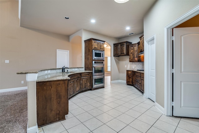 kitchen featuring light tile patterned flooring, dark brown cabinets, appliances with stainless steel finishes, light stone countertops, and decorative backsplash