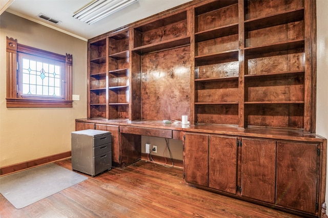 unfurnished office with built in desk, hardwood / wood-style floors, and crown molding