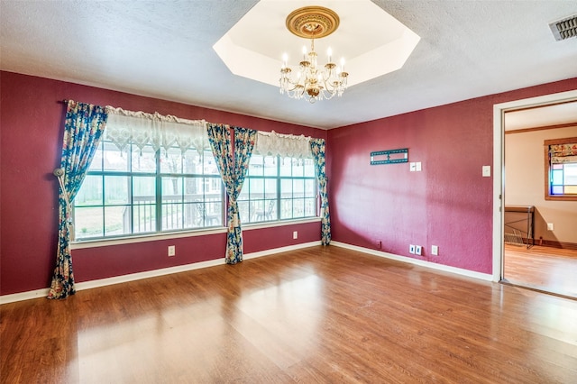 empty room with wood-type flooring, a chandelier, a raised ceiling, and a textured ceiling