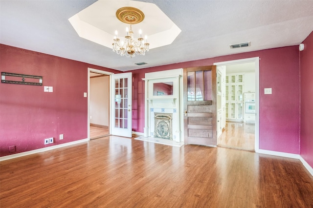 unfurnished living room with hardwood / wood-style flooring, a tray ceiling, an inviting chandelier, and a textured ceiling