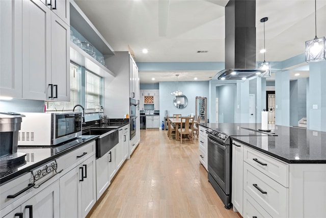 kitchen featuring stainless steel appliances, island range hood, white cabinets, and decorative light fixtures