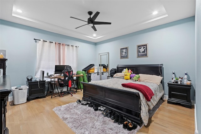 bedroom featuring ceiling fan, light wood-type flooring, and a tray ceiling