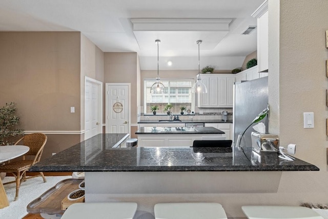 kitchen with white cabinetry, stainless steel refrigerator, kitchen peninsula, and a kitchen bar