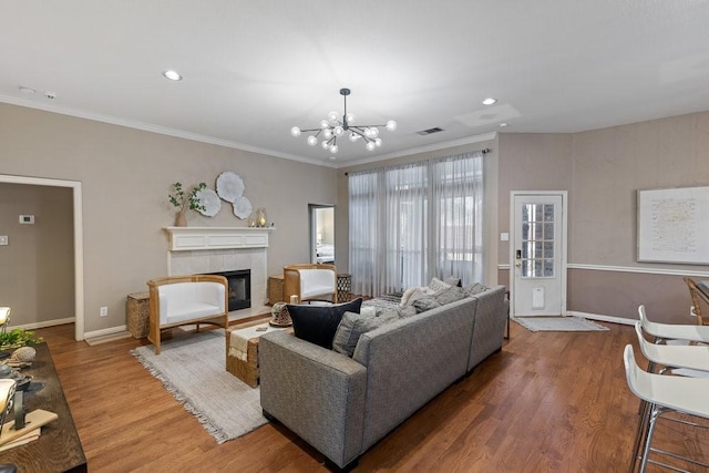 living room with crown molding, a chandelier, hardwood / wood-style floors, and a tile fireplace