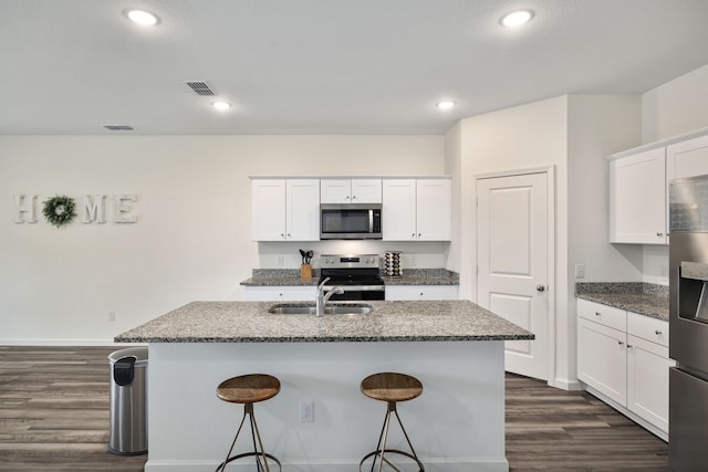 kitchen with white cabinetry, appliances with stainless steel finishes, a center island with sink, and dark stone countertops