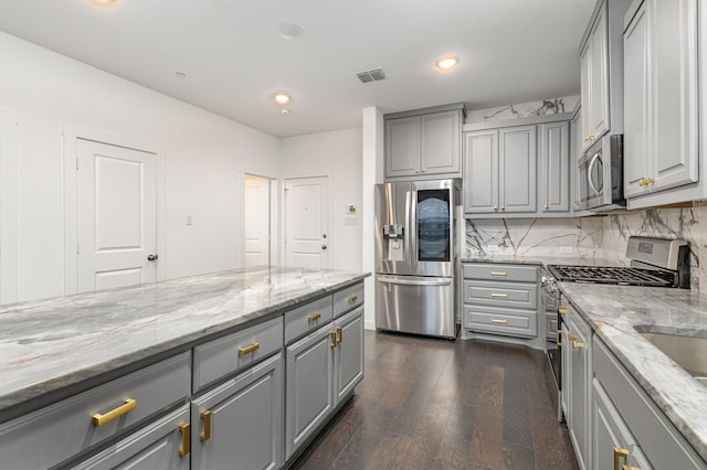 kitchen with gray cabinetry, light stone counters, appliances with stainless steel finishes, dark hardwood / wood-style floors, and decorative backsplash