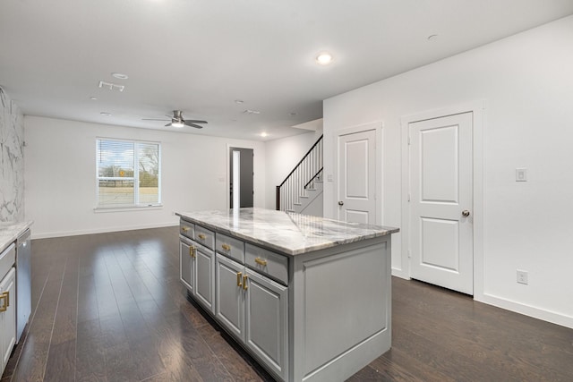 kitchen featuring dark wood-type flooring, gray cabinetry, a center island, dishwasher, and light stone countertops