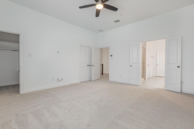 unfurnished bedroom featuring multiple closets, light colored carpet, ceiling fan, and a high ceiling