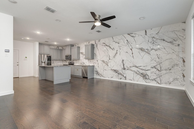 kitchen with a breakfast bar, appliances with stainless steel finishes, dark hardwood / wood-style flooring, gray cabinets, and a kitchen island