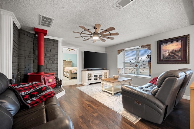 living room featuring a textured ceiling, dark wood-type flooring, ceiling fan, and a wood stove