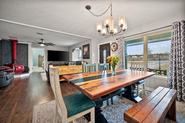 dining space featuring a wood stove, ceiling fan with notable chandelier, a textured ceiling, and dark hardwood / wood-style flooring