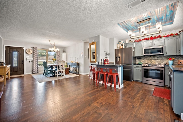 kitchen with dark wood-type flooring, gray cabinets, stainless steel appliances, a kitchen bar, and decorative backsplash