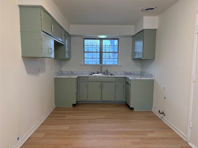 kitchen with green cabinets, sink, and light wood-type flooring