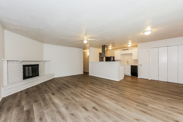 unfurnished living room featuring ceiling fan, a fireplace, sink, and light wood-type flooring