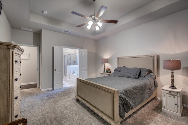 carpeted bedroom featuring a raised ceiling, connected bathroom, and ceiling fan