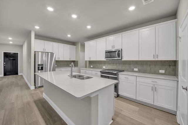 kitchen with sink, white cabinetry, light hardwood / wood-style flooring, stainless steel appliances, and a kitchen island with sink