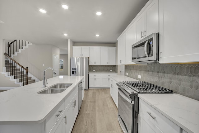 kitchen featuring sink, white cabinets, a kitchen island with sink, stainless steel appliances, and light stone countertops