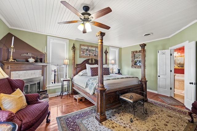 bedroom featuring a tiled fireplace, hardwood / wood-style flooring, ensuite bath, and ornamental molding