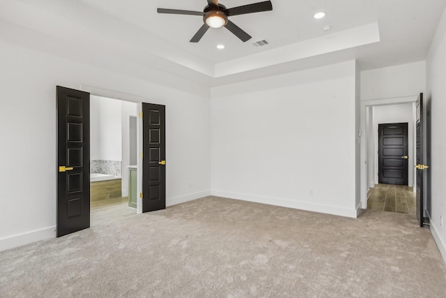 unfurnished bedroom with ceiling fan, light colored carpet, and a tray ceiling