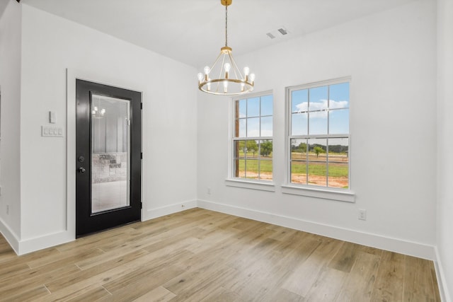 spare room featuring a notable chandelier and light wood-type flooring