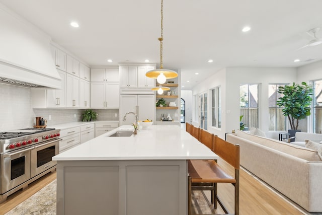 kitchen with a breakfast bar, premium appliances, white cabinets, decorative light fixtures, and custom exhaust hood