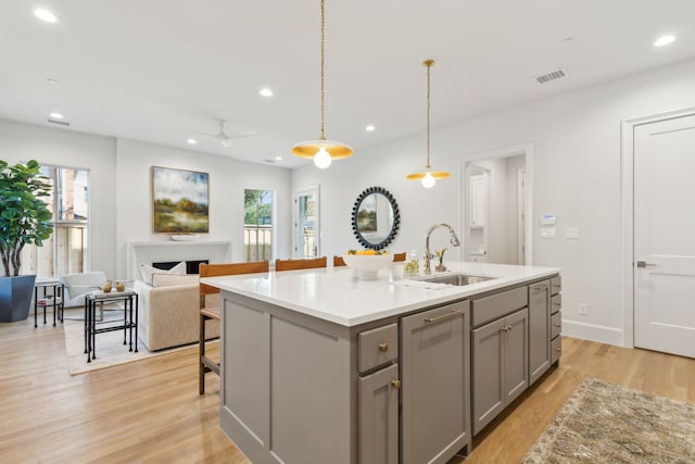 kitchen with sink, gray cabinetry, hanging light fixtures, a kitchen island with sink, and light hardwood / wood-style flooring