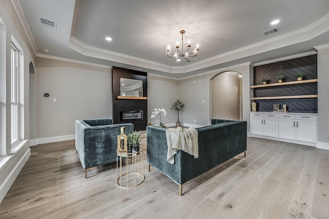 living area with a large fireplace, visible vents, arched walkways, a tray ceiling, and light wood-type flooring