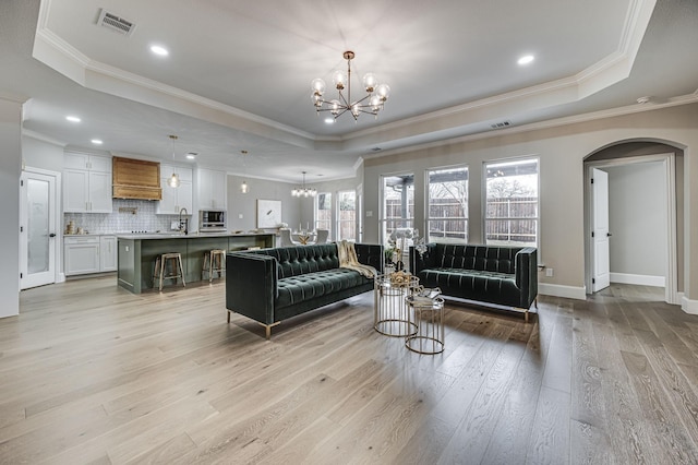 living room with light wood-style flooring, a raised ceiling, visible vents, and an inviting chandelier