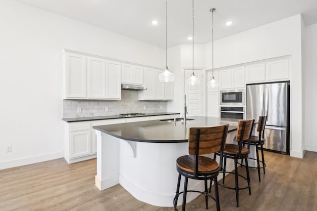 kitchen with an island with sink, pendant lighting, stainless steel appliances, decorative backsplash, and white cabinets