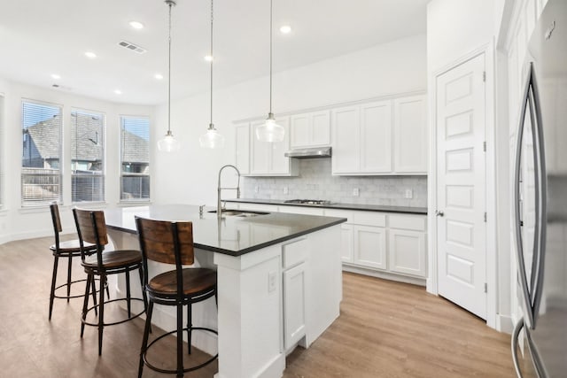 kitchen featuring sink, a kitchen island with sink, hanging light fixtures, stainless steel appliances, and white cabinets