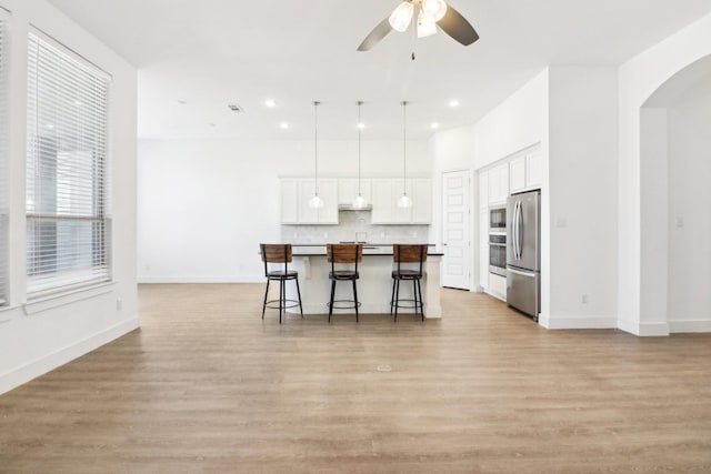 kitchen with appliances with stainless steel finishes, a breakfast bar, white cabinets, hanging light fixtures, and a center island with sink