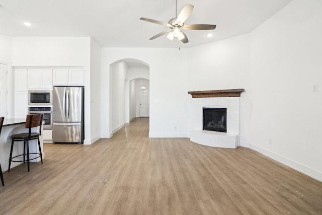 unfurnished living room with ceiling fan, a brick fireplace, and light wood-type flooring