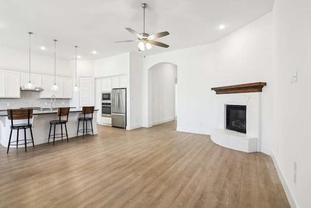 living room with a fireplace, sink, a high ceiling, ceiling fan, and light hardwood / wood-style flooring