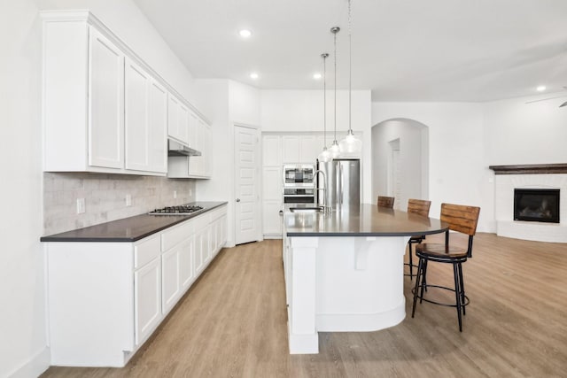 kitchen with a kitchen bar, white cabinetry, a center island with sink, stainless steel appliances, and backsplash