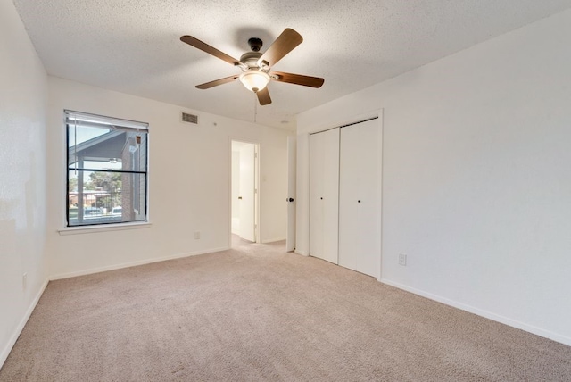 unfurnished bedroom featuring ceiling fan, a closet, light carpet, and a textured ceiling