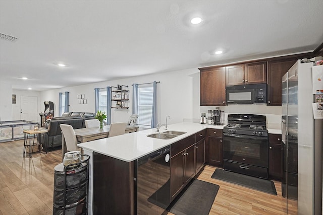 kitchen featuring dark brown cabinetry, sink, light wood-type flooring, kitchen peninsula, and black appliances