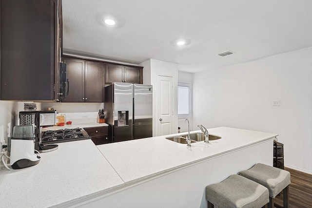 kitchen featuring appliances with stainless steel finishes, dark hardwood / wood-style floors, sink, dark brown cabinetry, and kitchen peninsula