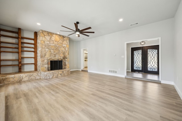 unfurnished living room with french doors, ceiling fan, a fireplace, and light hardwood / wood-style floors