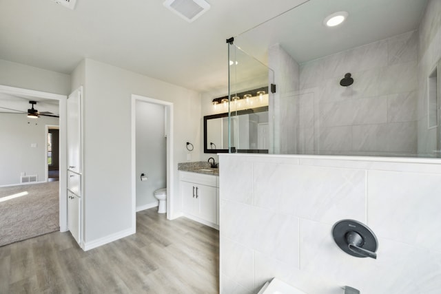 bathroom featuring a tile shower, wood-type flooring, vanity, ceiling fan, and toilet